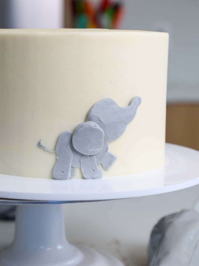 image of a baby elephant being added to the side of a cake with gray buttercream