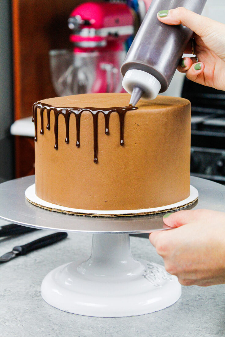 image of chocolate ganache drips being added to a chocolate drip cake using a plastic bottle