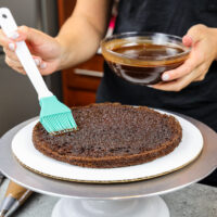 image of a chocolate cake layer being soaked with chocolate simple syrup