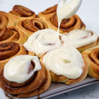 image of a mini cinnamon roll being frosted with cream cheese frosting