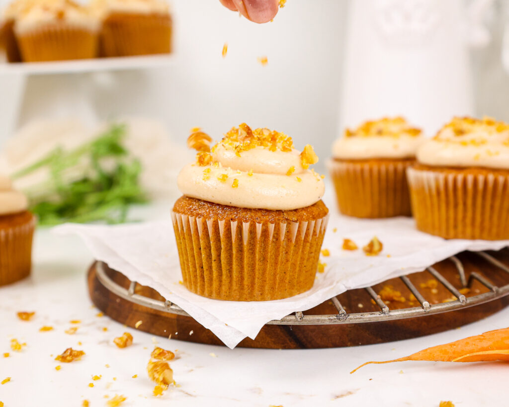 image of carrot cake cupcakes being topped with a spiced cream cheese frosting a crunchy walnut brittle