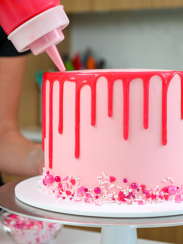 image of hot pink ganache drips being added around a pink bubblegum cake