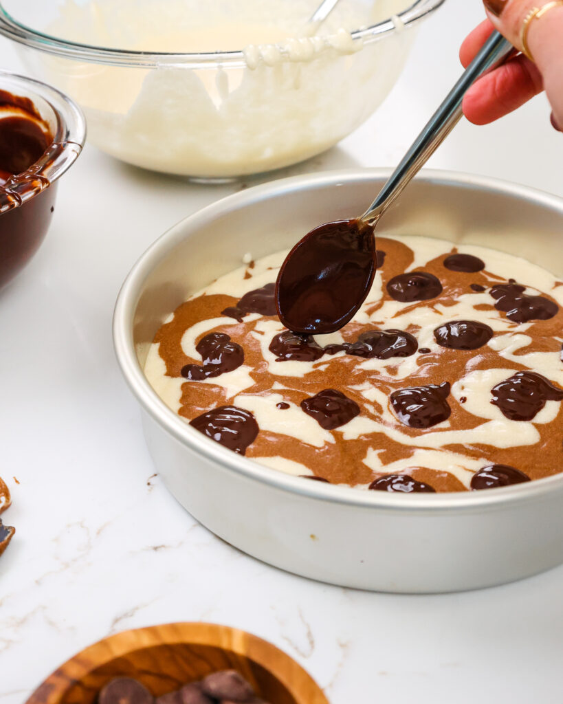 image of chocolate fudge being added into marble cake layers to make a fudge ripple swirl