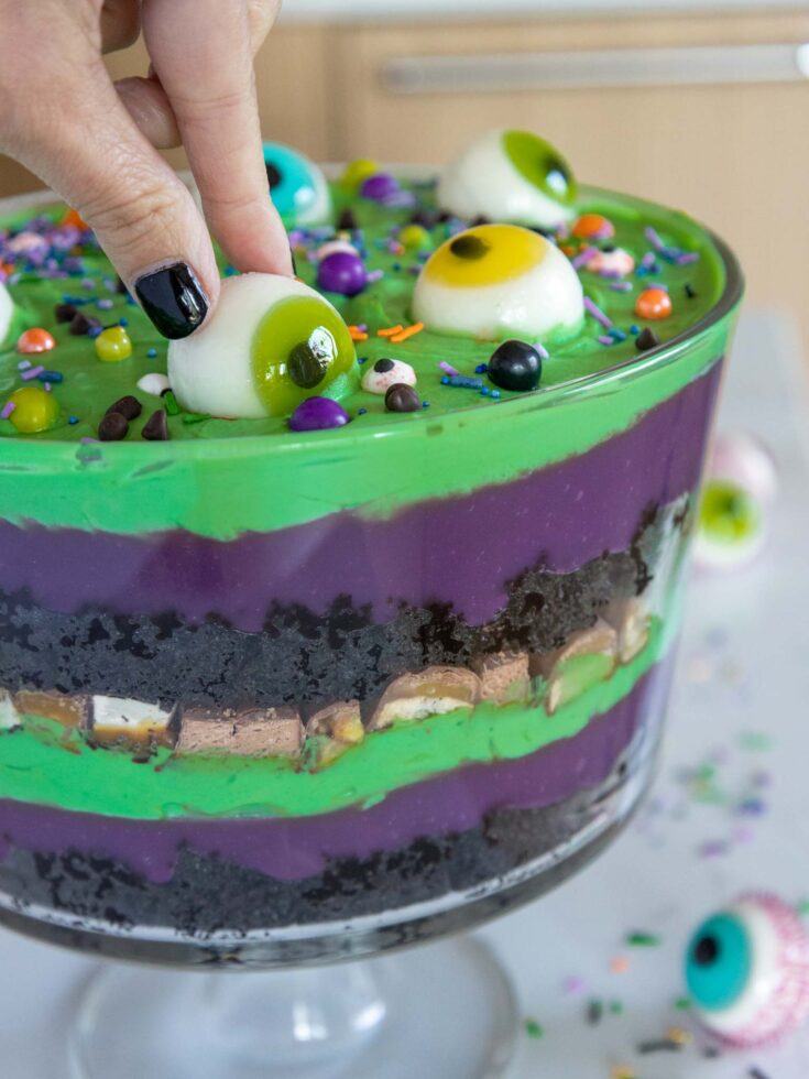 image of a halloween trifle made with purple and green pudding and whipped cream and decorated with gummy eyeballs and halloween sprinkles