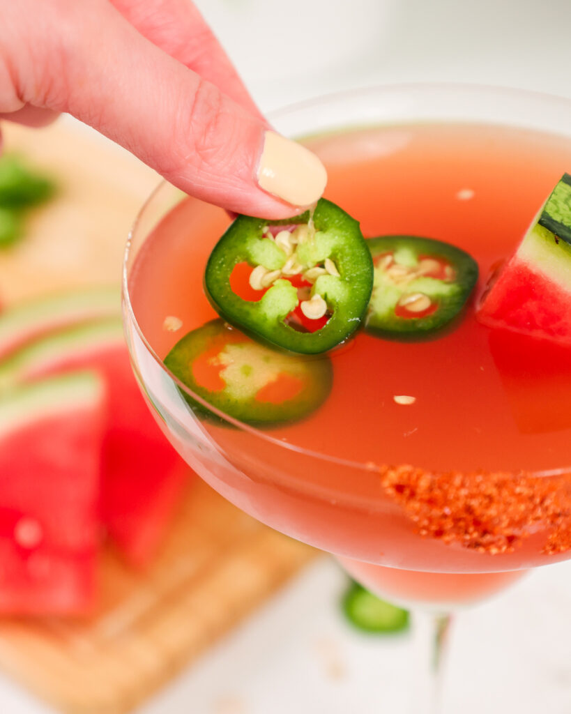 image of a spicy watermelon margarita being garnished with jalapeño coins