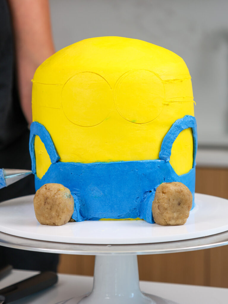 image of buttercream overalls being piped onto a minions cake with blue buttercream