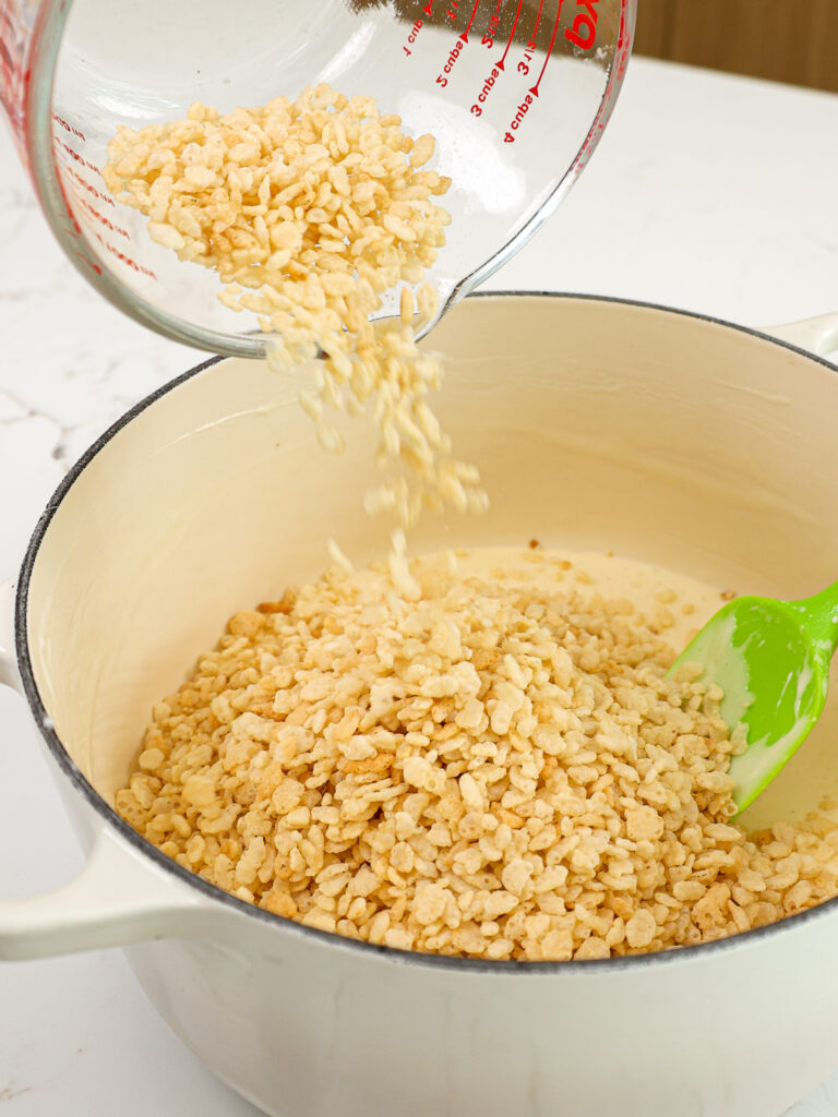 image puffed rice cereal being poured into a pot of melted marshmallows and butter