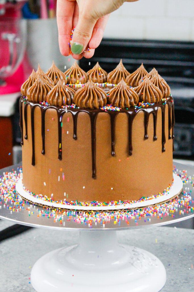 image of rainbow sprinkles being added to a chocolate drip cake