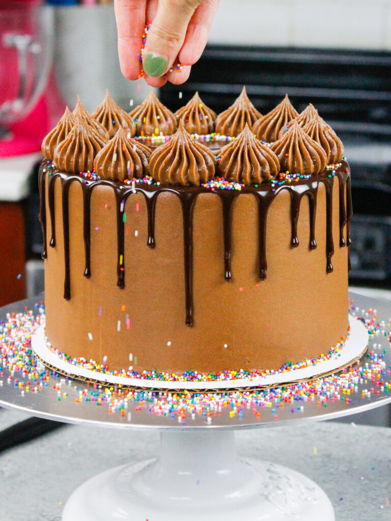 image of rainbow sprinkles being added to a chocolate drip cake