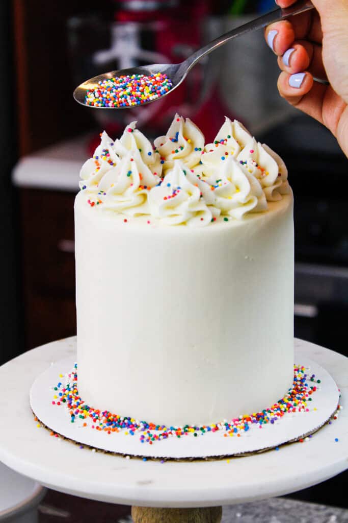 image of mini vanilla cake being decorated with rainbow sprinkles for a birthday