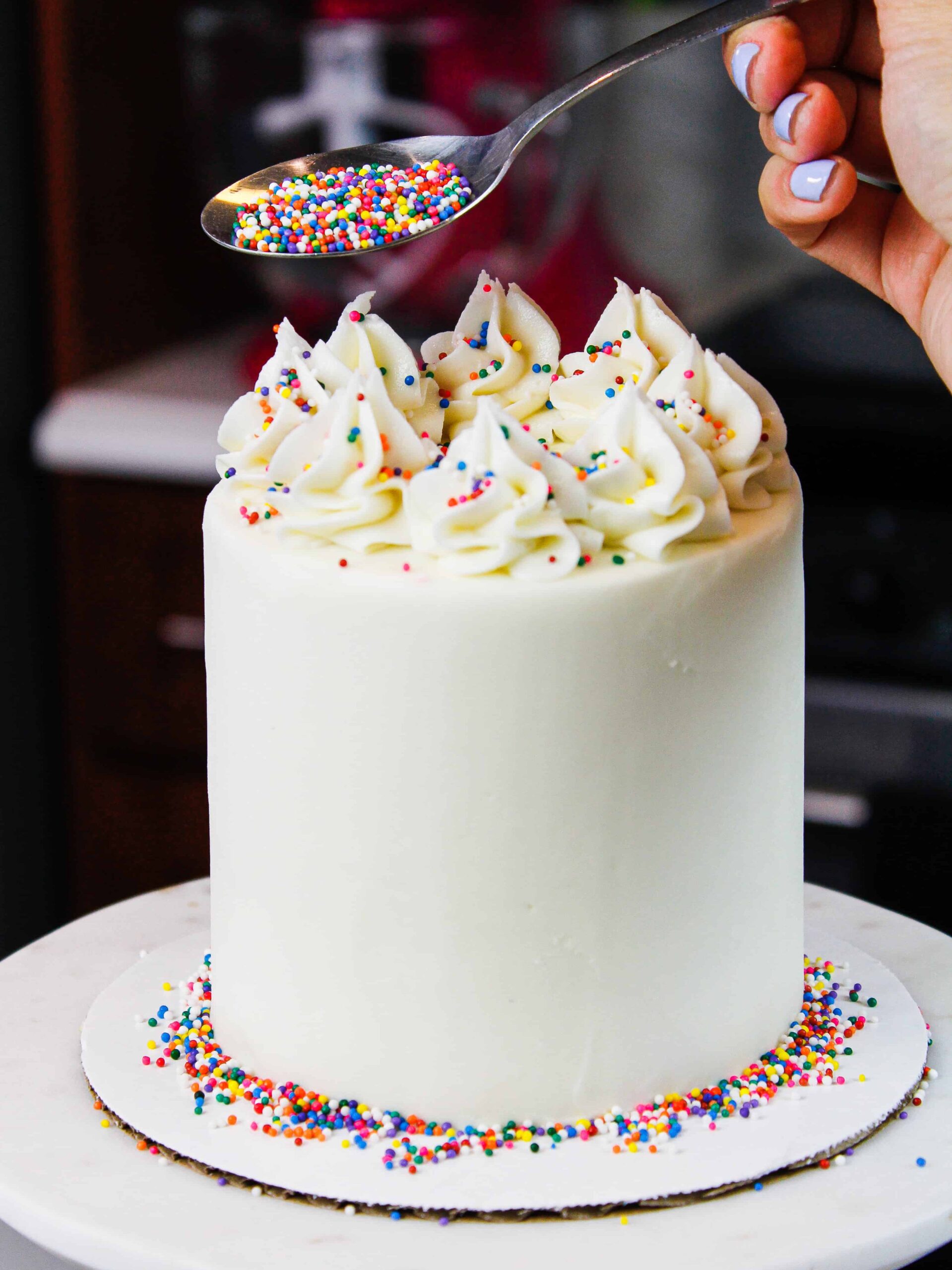 image of mini vanilla cake being decorated with rainbow sprinkles for a birthday