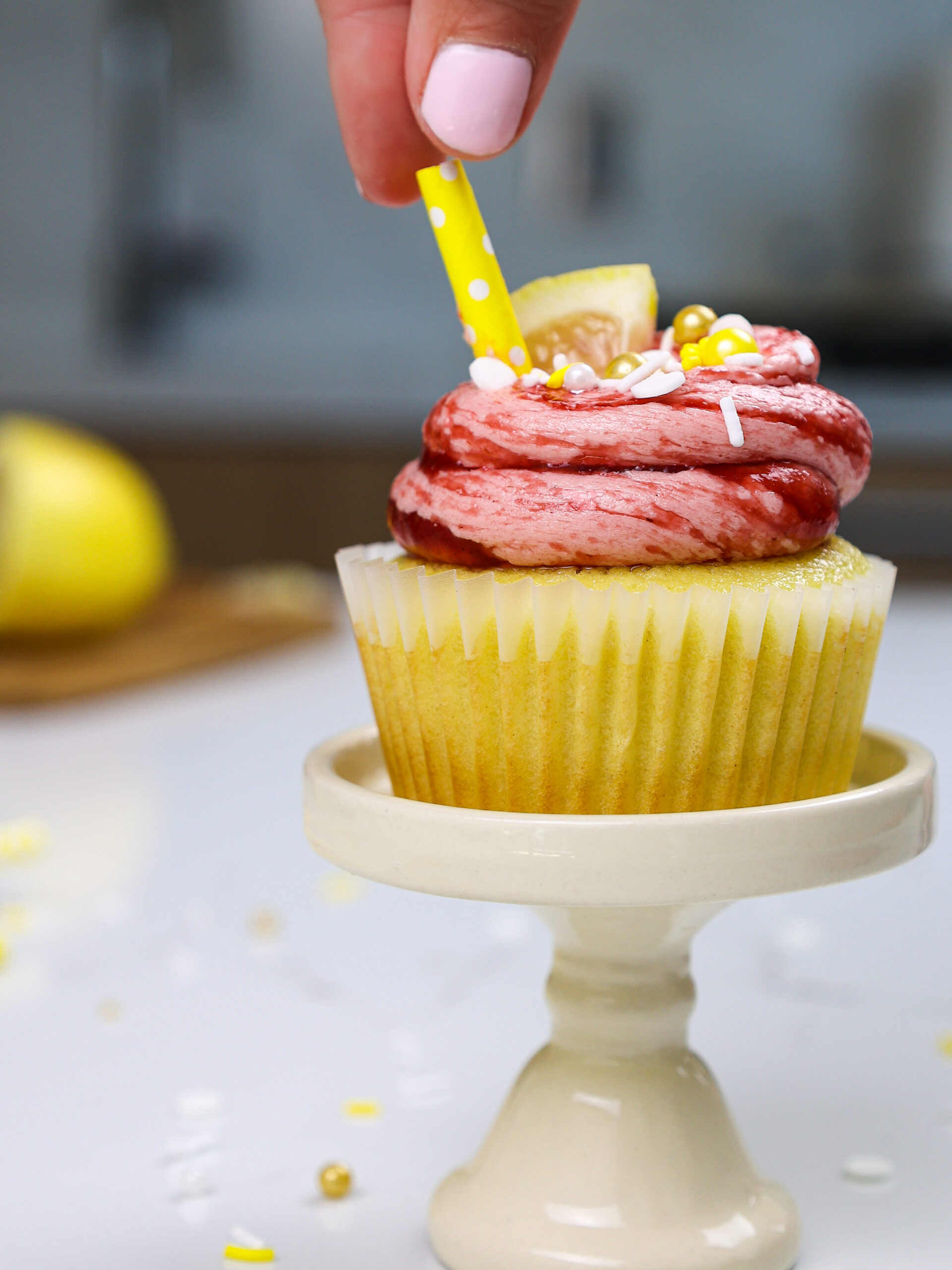 image of a straw being added as a garnish to a lemon raspberry cupcake