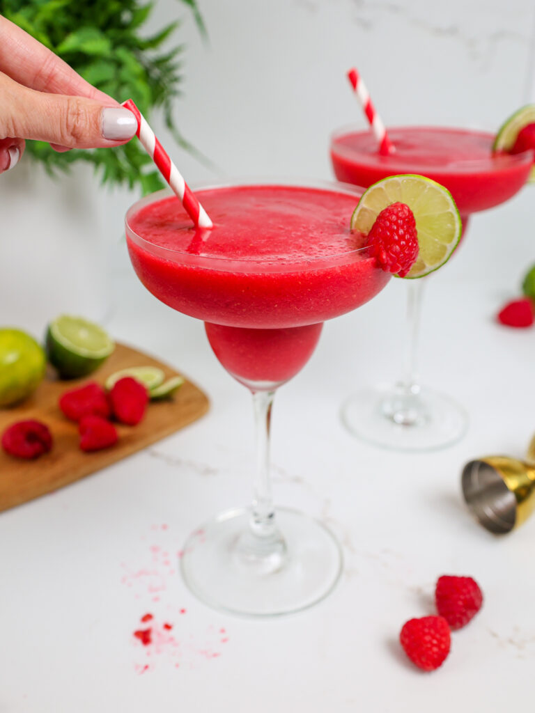 image of a frozen raspberry daiquiri that's been poured into a margarita glass and served with a fun matching straw
