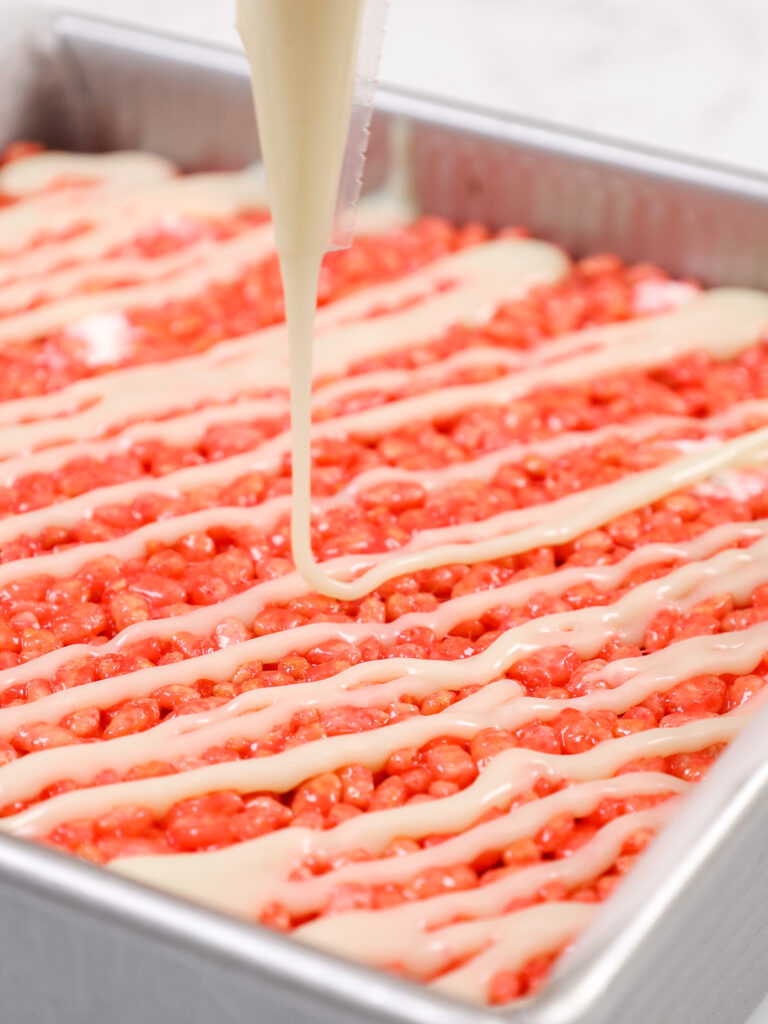 image of white chocolate ganache being drizzled on top of strawberry rice krispie treats in a pan