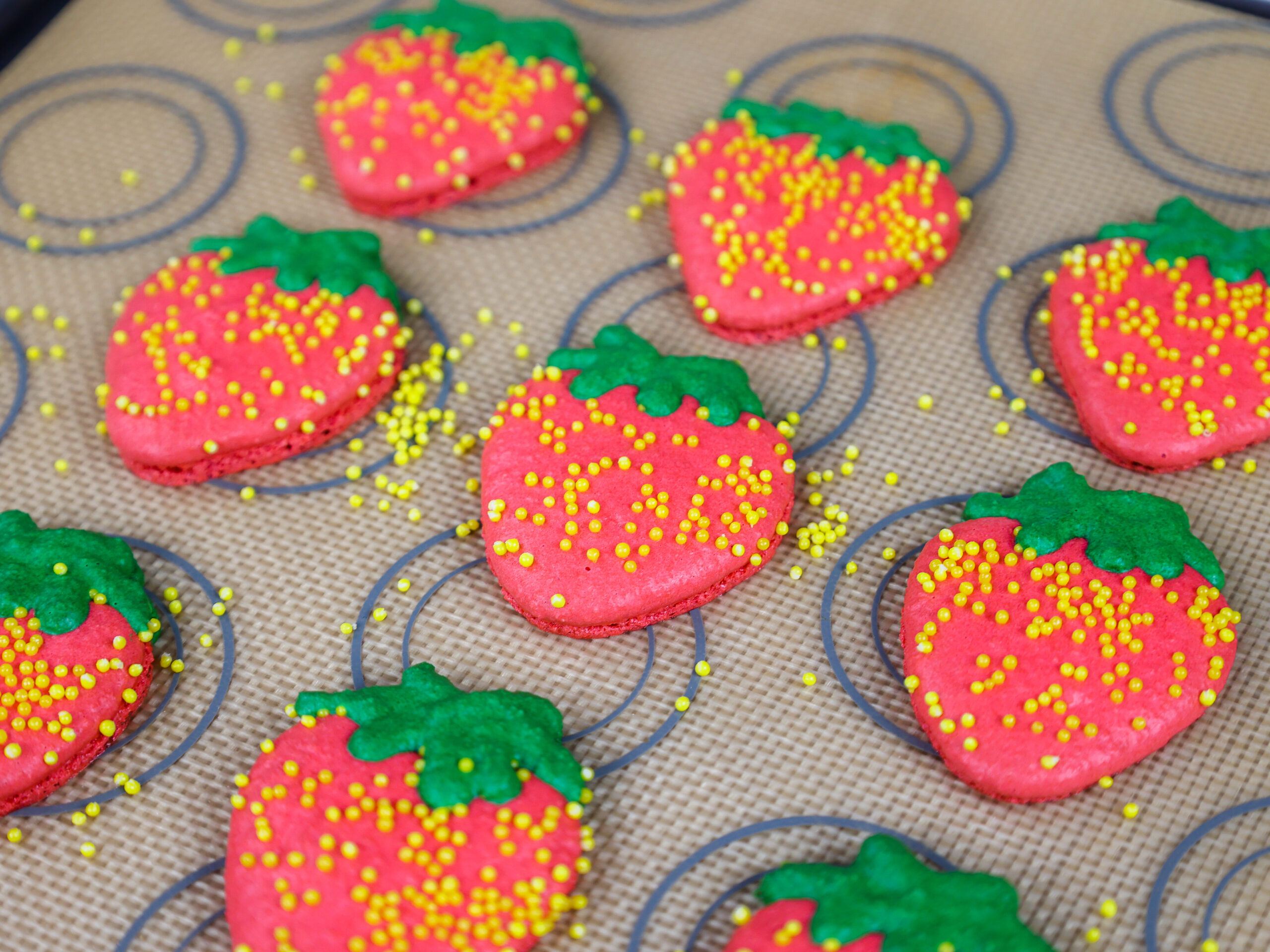 image of strawberry shaped macaron shells that have been baked and have nice feet and are shared as part of a macaron round up post