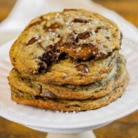 image of brown butter Nutella chocolate chip cookies in a stack with the top cookie bitten into showing the warm, melting nutella