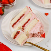 image of a slice of a vanilla and strawberry cake on a plate that's been cut into with a fork