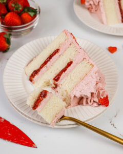 image of a slice of a vanilla and strawberry cake on a plate that's been cut into with a fork