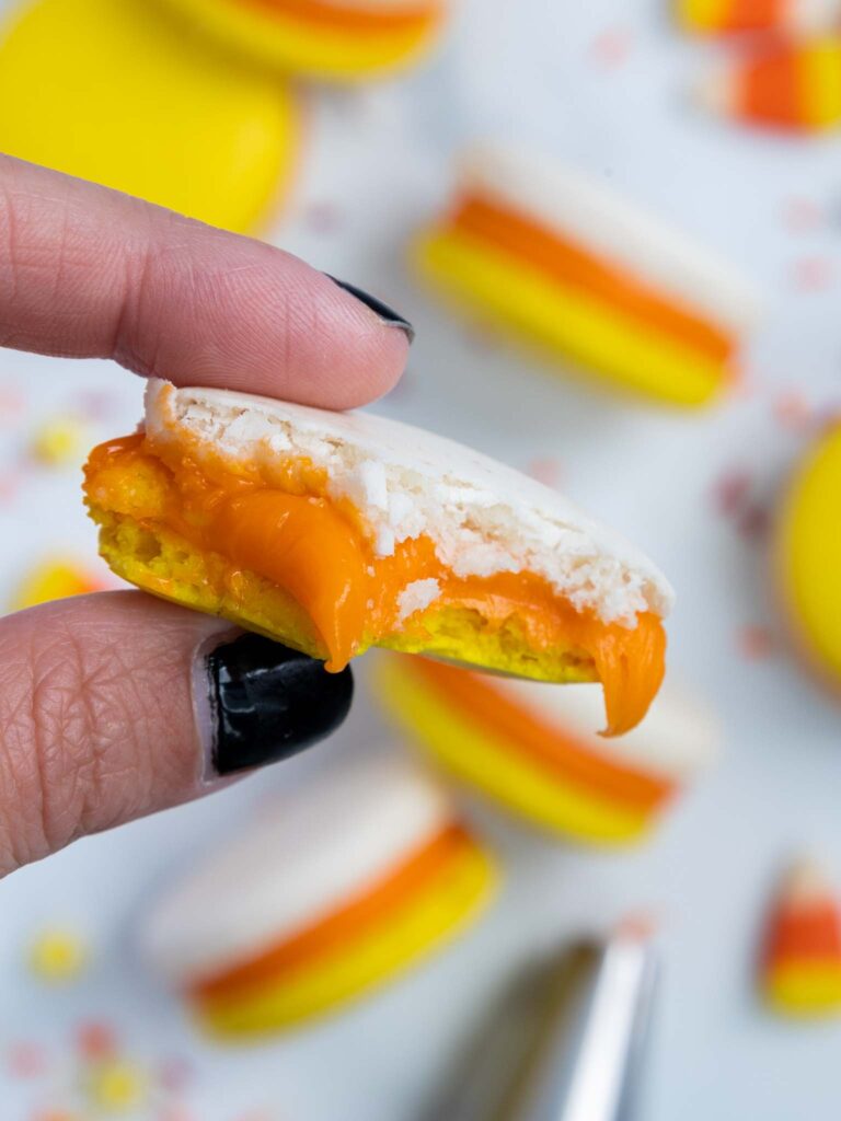 image of a candy corn macaron that's been bitten into to show it's delicious candy corn ganache