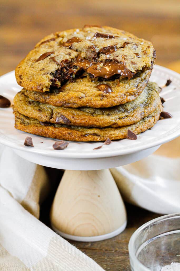 image of stack of brown butter nutella stuffed chocolate chip cookies, with the top cookie bitten into with nutella oozing out