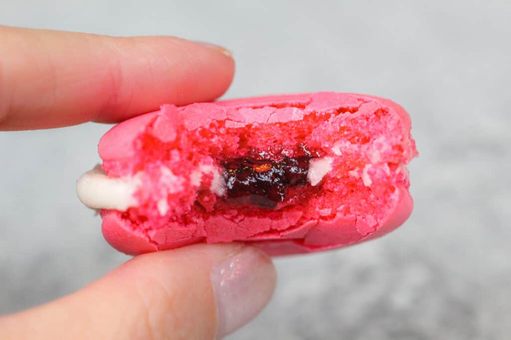 image of a raspberry macaron that's been bitten into to show it's raspberry jam filling
