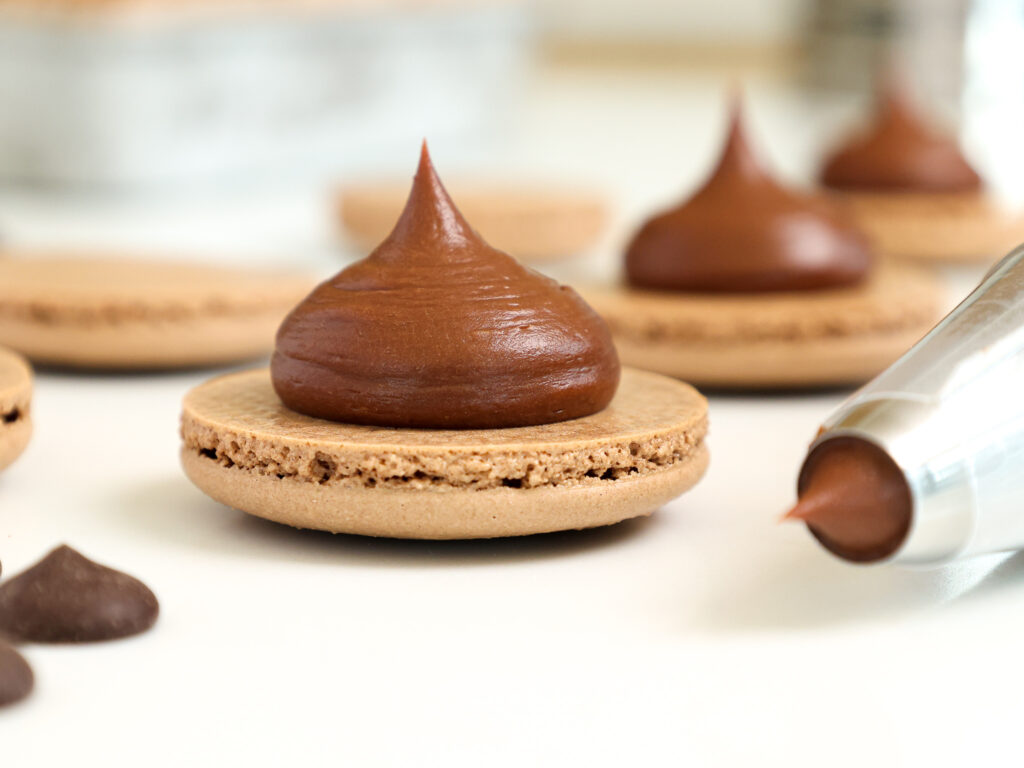 image of a french chocolate macaron being filled with a semi sweet chocolate ganache