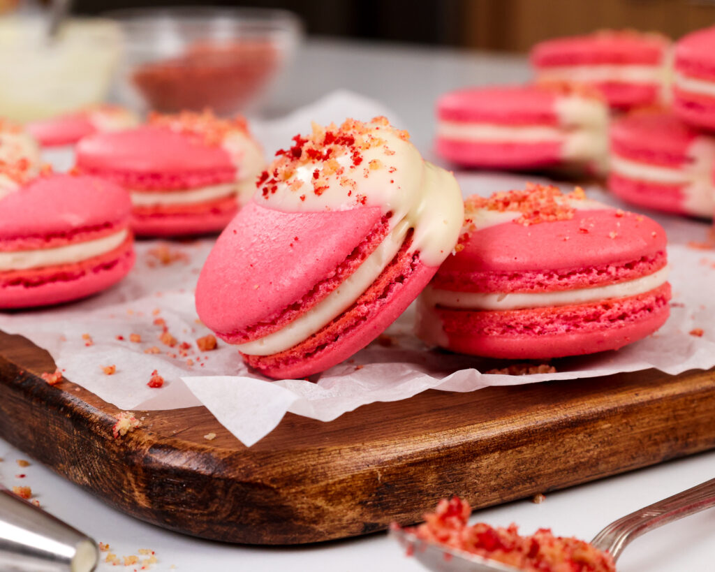 image of strawberry shortcake macarons that have been filled with strawberry jam and a mascarpone filling and topped with a strawberry shortcake crumble