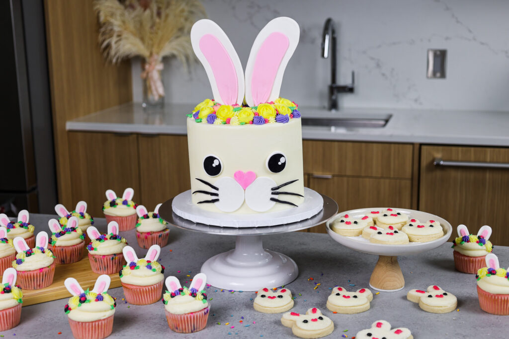 image of a bunny birthday cake made with funfetti cake layers and homemade vanilla buttercream made with matching bunny cookies and cupcakes for a bunny themed party
