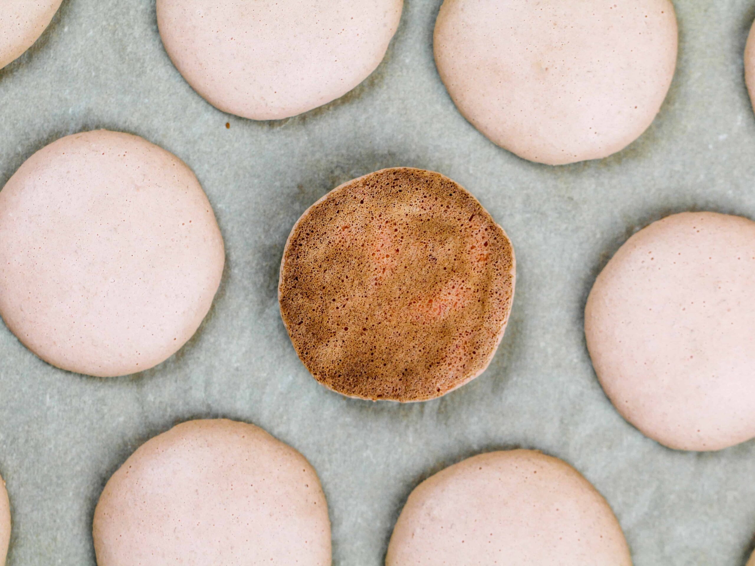 image of an overcooked macaron shell that has a brown bottom included in a macaron troubleshooting guide explaining how to avoid this issue