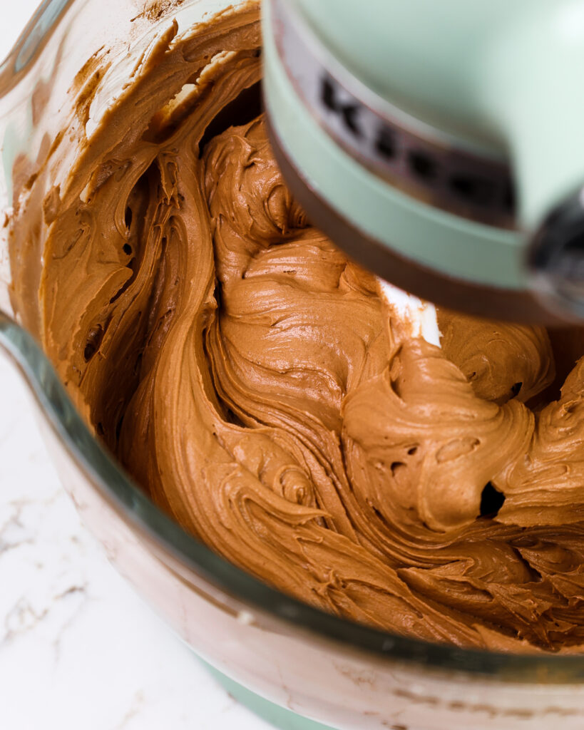 image of chocolate buttercream being mixed in a KitchenAid stand mixer