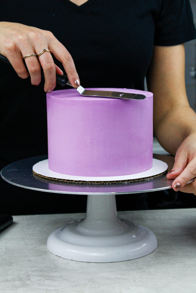 image of a buttercream cake being frosted with sharp edges and smooth sides to show How to Frost a Cake Smoothly