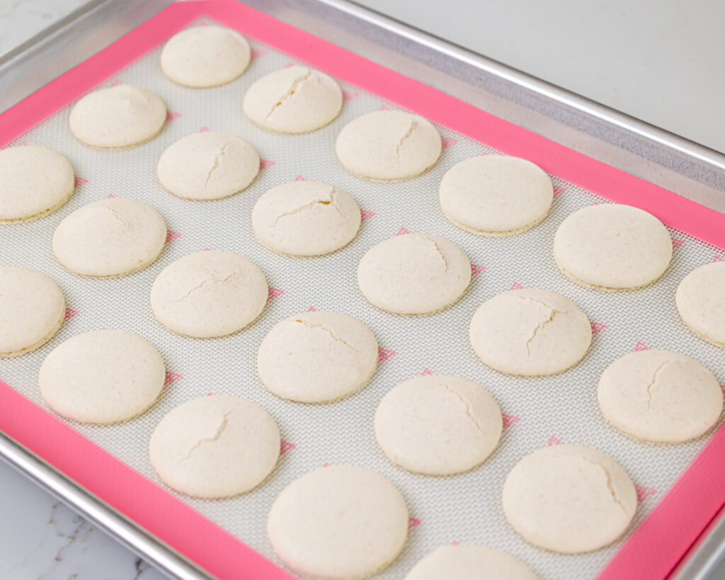 image of white macaron shells that have cracked because the oven was too hot