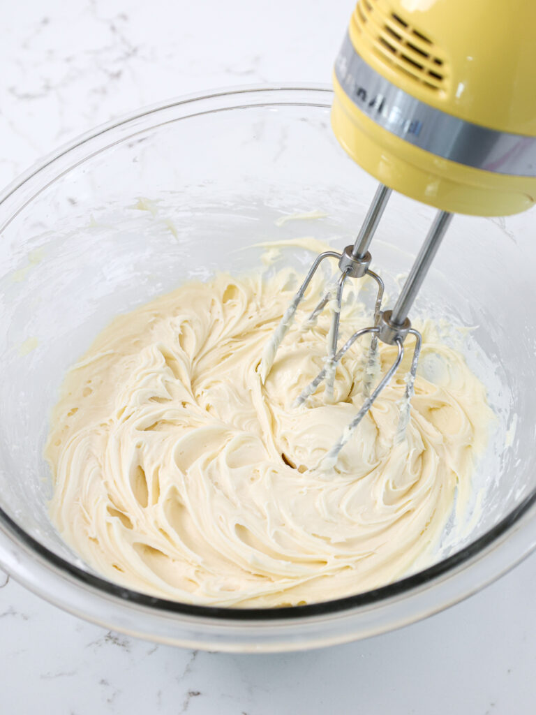image of cream cheese frosting being mixed in a glass bowl with a hand mixer