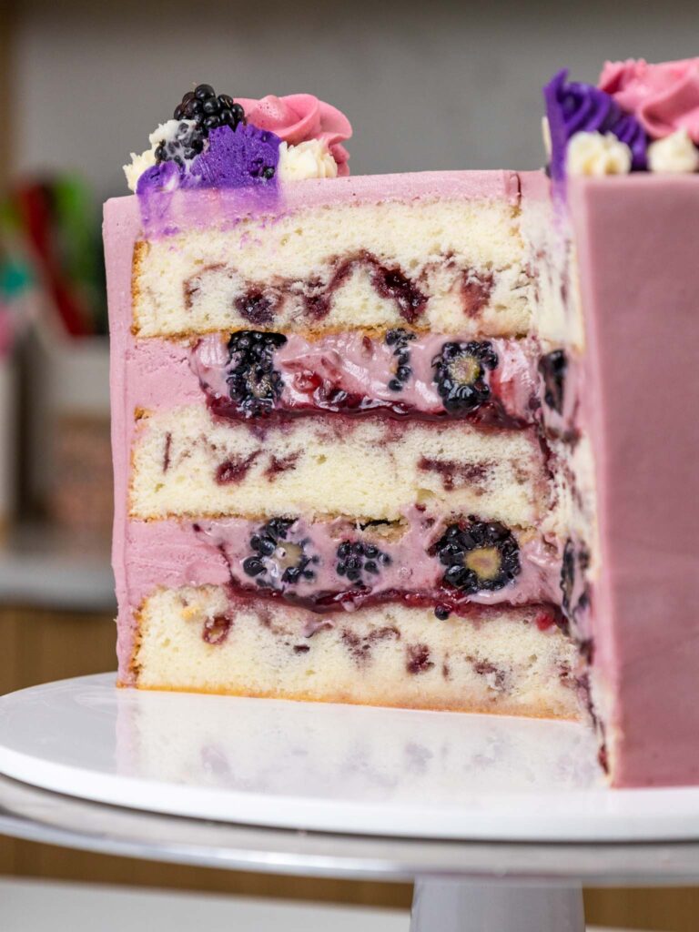 image of a blackberry mousse cake that's been cut into to show its blackberry swirled cake layers, blackberry mousse filling, and blackberry buttercream frosting
