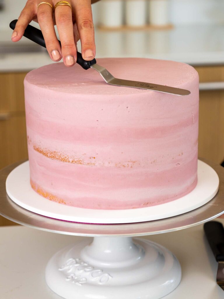 image of a blackberry mousse cake being crumb coated with blackberry frosting