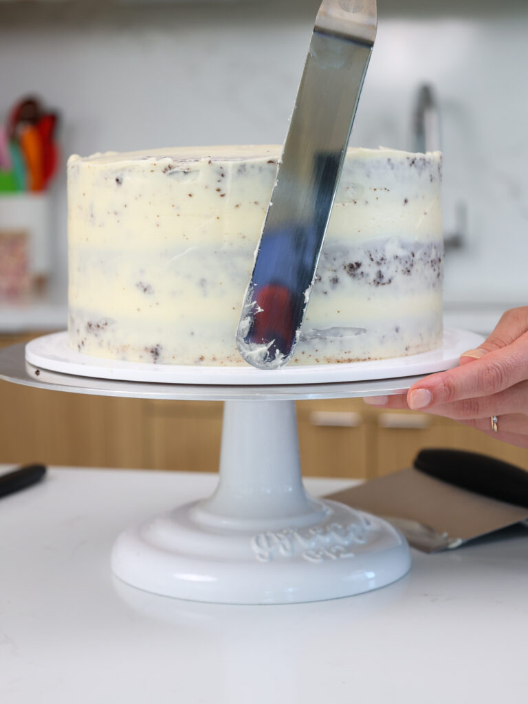 image of a chocolate cake being filled and crumb coated with cream cheese frosting 