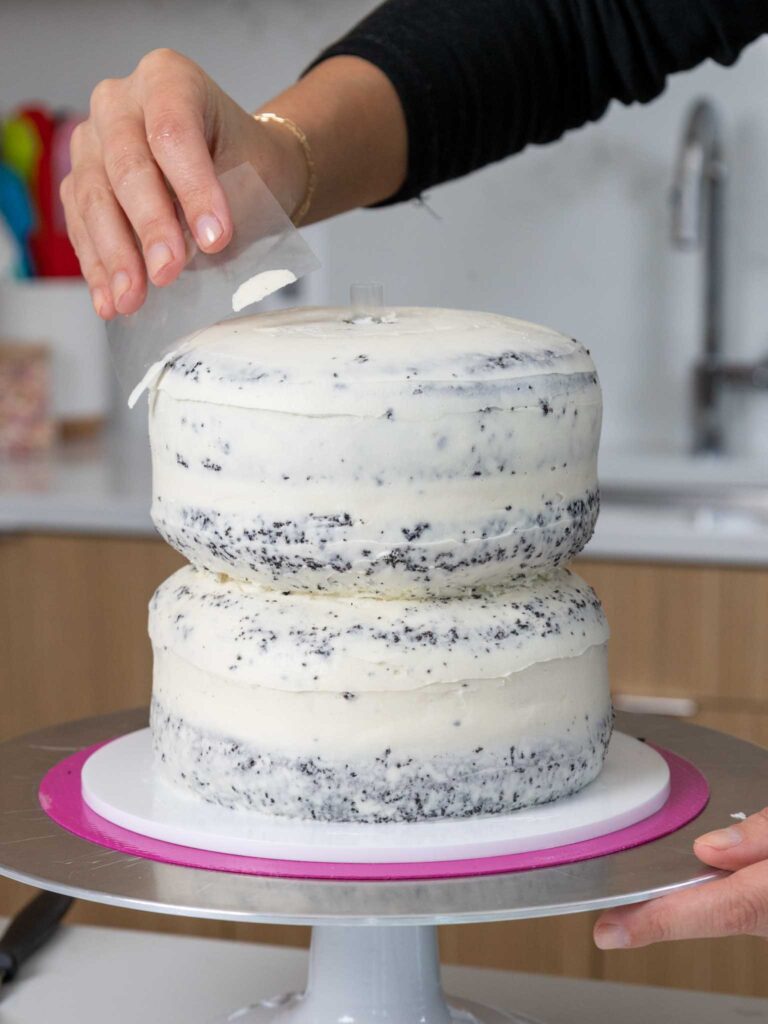 image of dark chocolate cake layers being crumb coated with vanilla buttercream to make a penguin cake