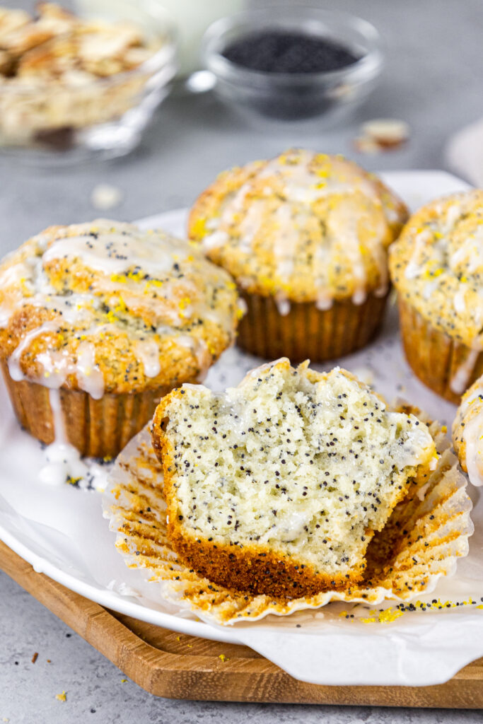 image of almond poppy seed muffins glazed with almond glaze sitting on a tray with one cut open to show how fluffy and tender the inside is