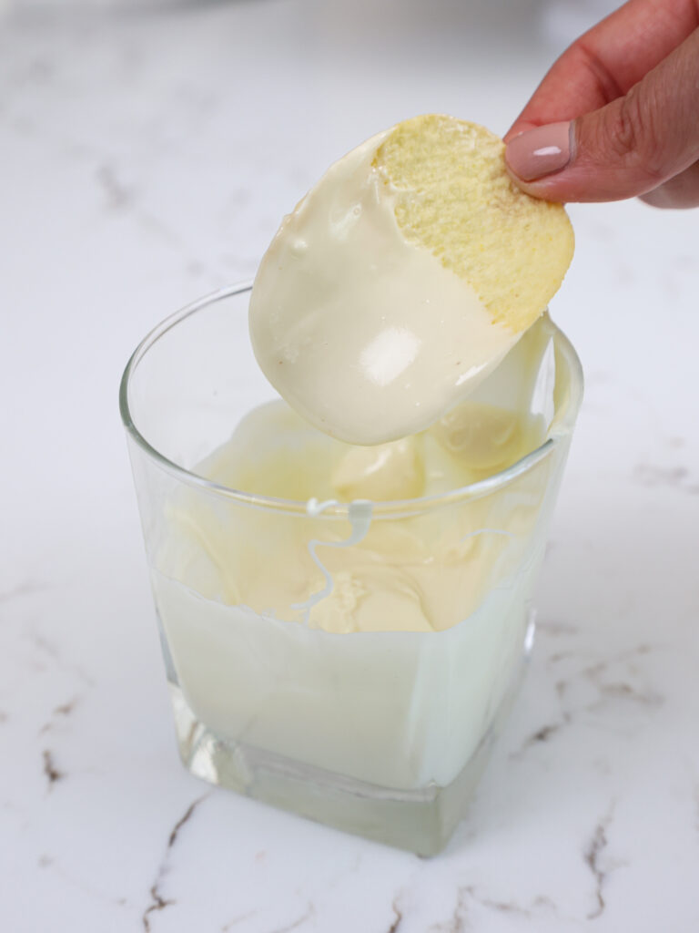 image of a Pringle chip being dipped into white chocolate to be the ears on a llama cake