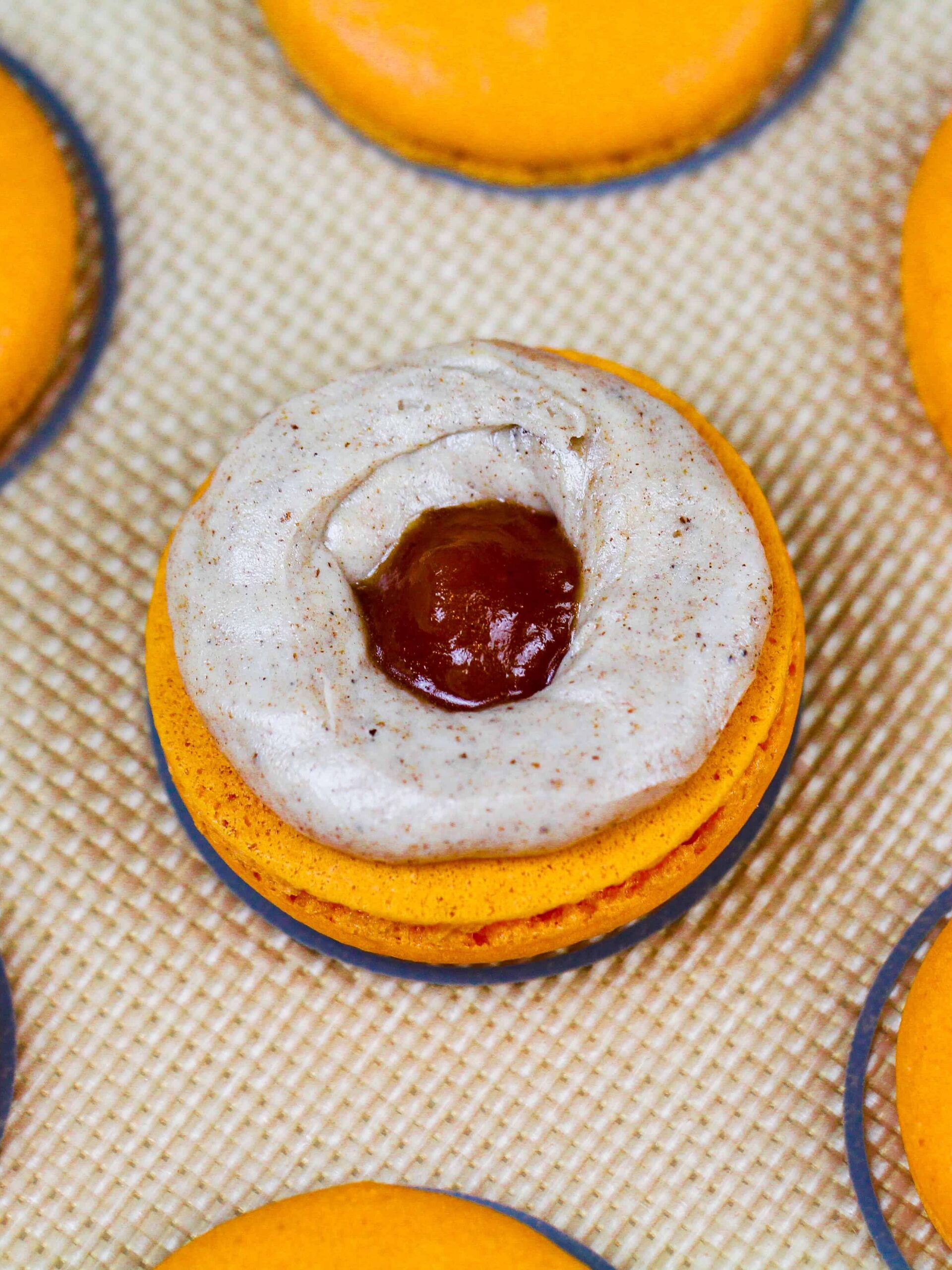 image of a pumpkin macaron being filled with spiced buttercream and pumpkin pie filling