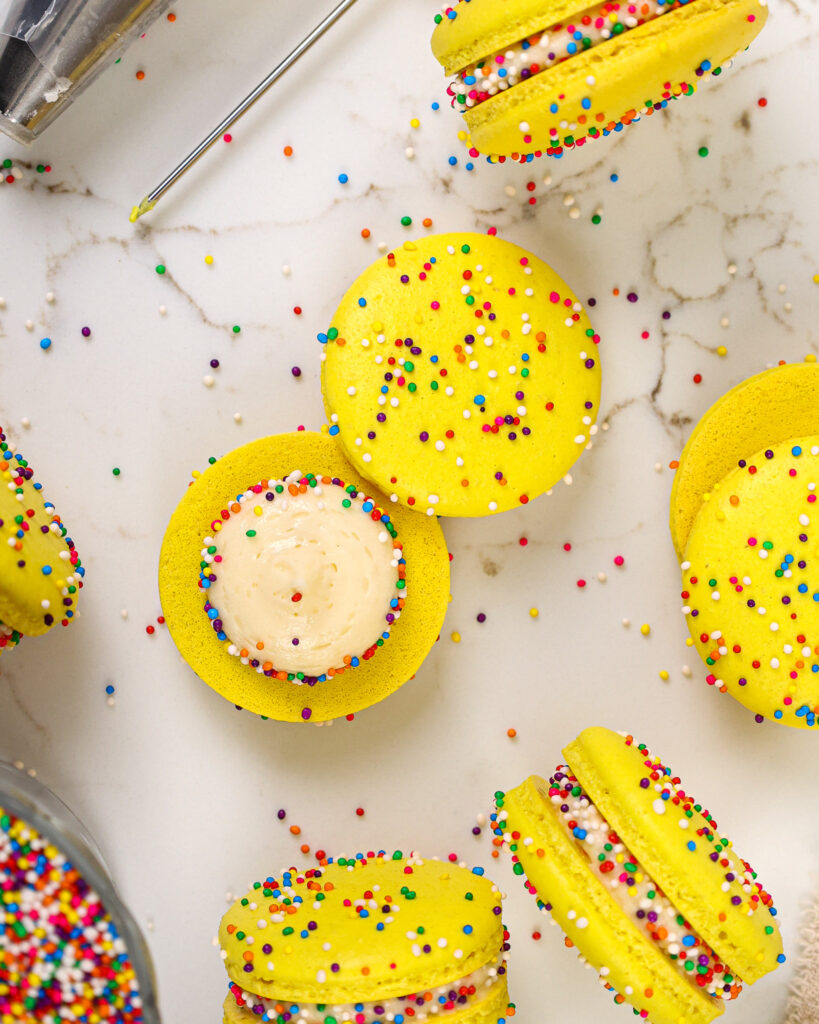 image of a funfetti macaron being filled with cream cheese frosting and rainbow sprinkles