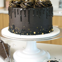 image of a black drip cake that's been decorated with gold sprinkles and edible gold paint