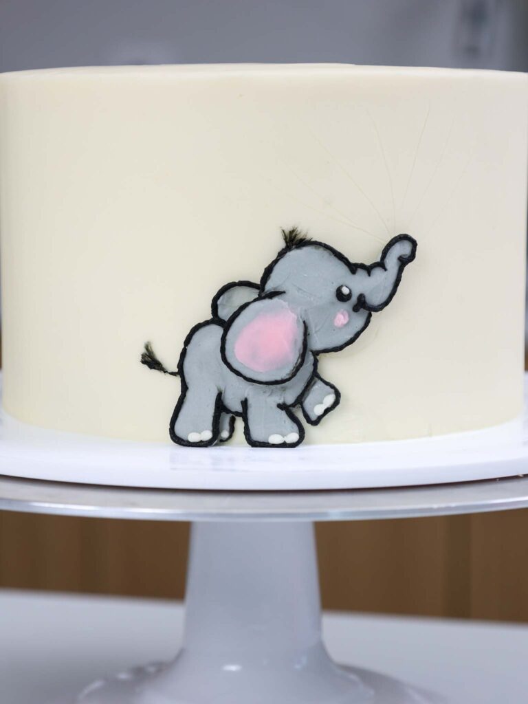 image of a baby elephant being added to the side of a cake with gray buttercream