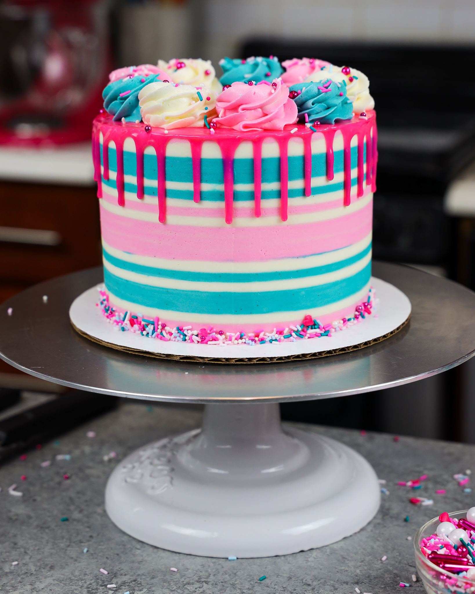 image of a gluten free funfetti cake that's been decorating with buttercream stripes and a pink drip