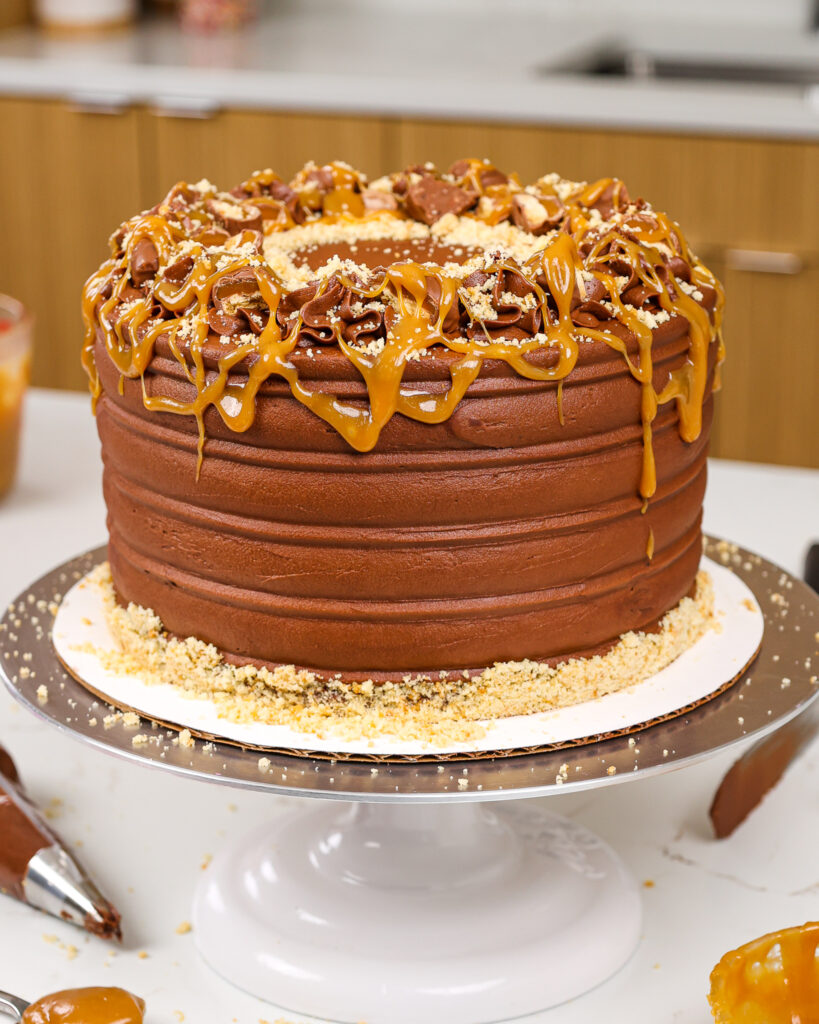 image of a twix cake that's been decorated with caramel, shortbread crumbs and chopped up twix