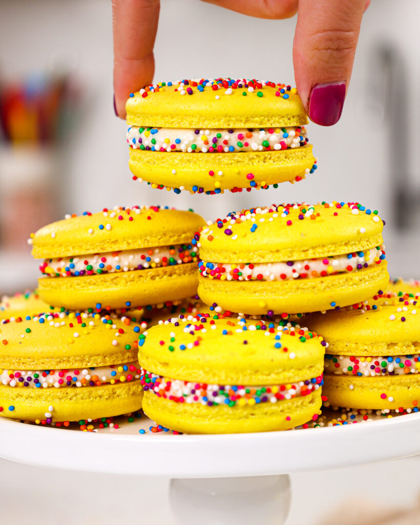 image of funfetti macarons being stacked on a plate that have been decorated with colorful nonpareil sprinkles