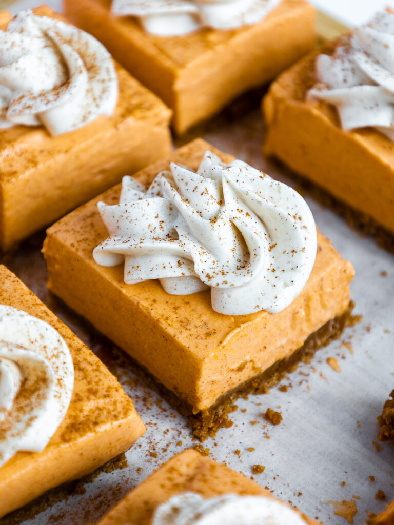 image of no bake pumpkin cheesecake bars that have been cut into squares and topped with whipped cream