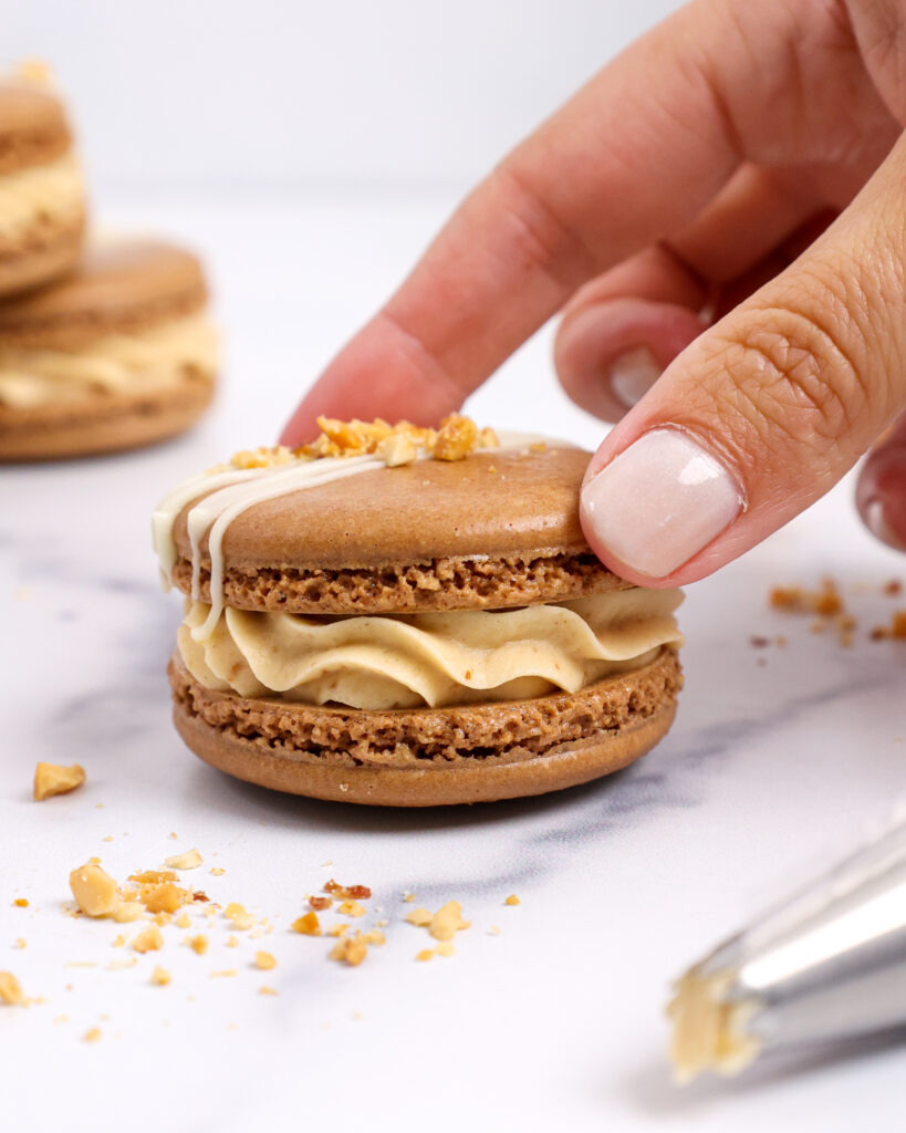 image of peanut butter macarons filled with honey roasted peanut butter buttercream and topped with chopped peanuts and a white chocolate drizzle