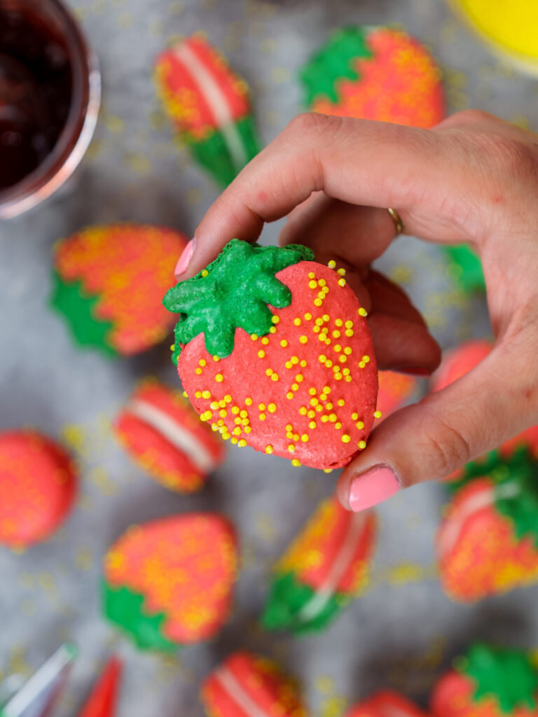 image of a strawberry shaped french macaron held up to show it's adorable shape