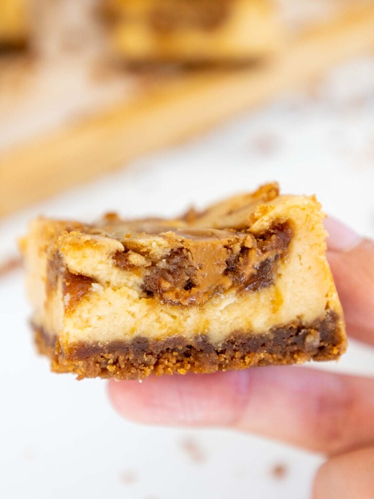 image of a biscoff cheesecake square being held up to show it's cross section